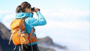 Hiker with binoculars scanning the horizon above clouds.