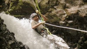 Person rappelling down a waterfall with climbing gear.