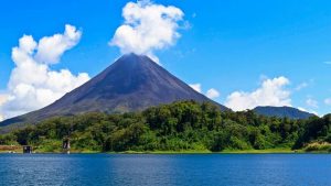 A majestic conical volcano looming over a tropical lake under a blue sky with clouds.