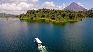 Boat cruising on a clear lake with a volcano in the background and lush greenery.